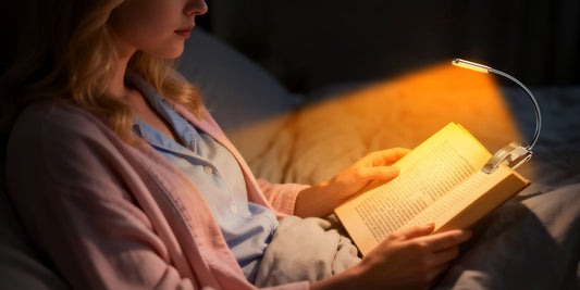 Woman reading in bed with a compact and lightweight amber LED book light clipped to her paperback.
